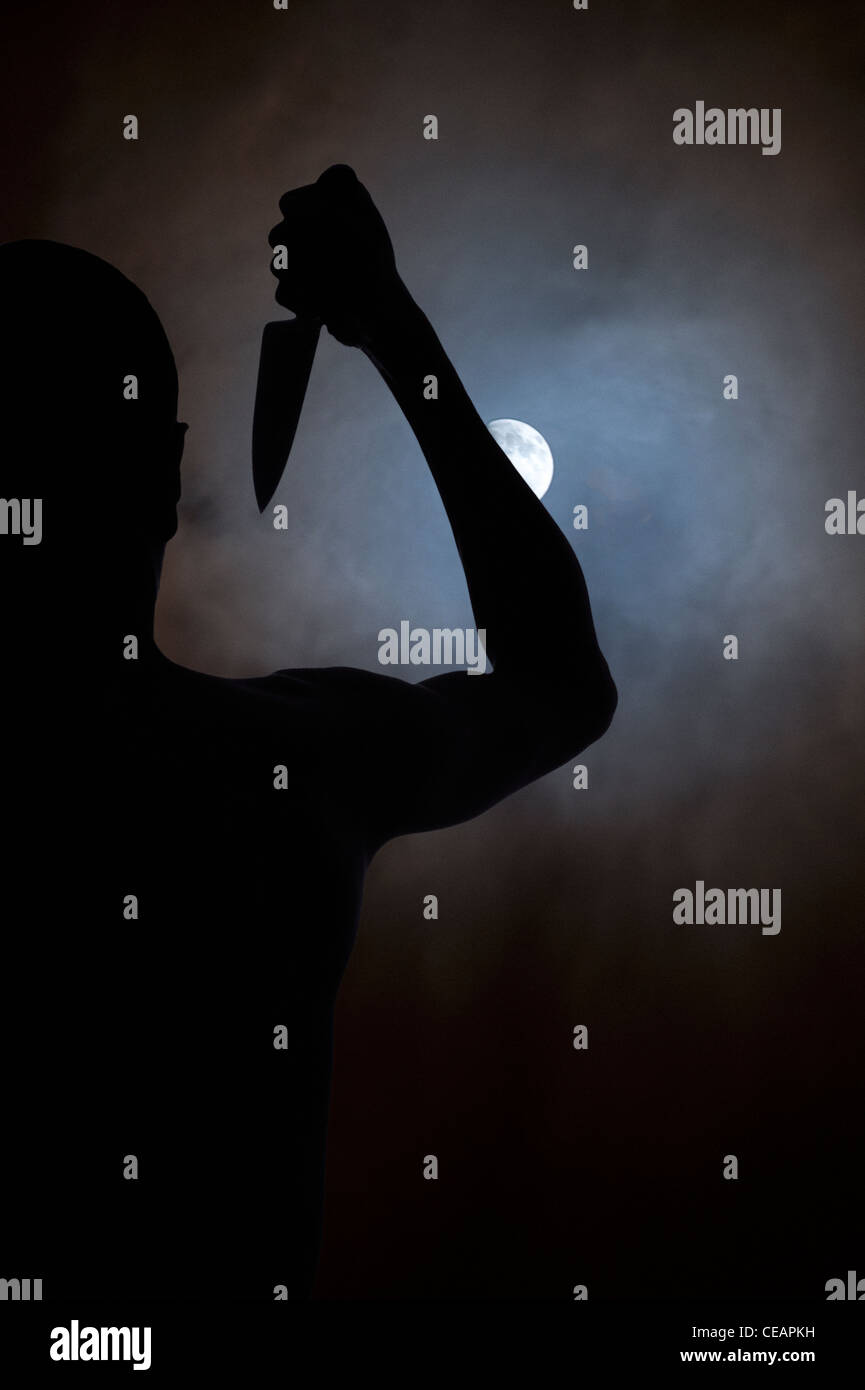 Silhouette of man with a knife looking at the moon Stock Photo