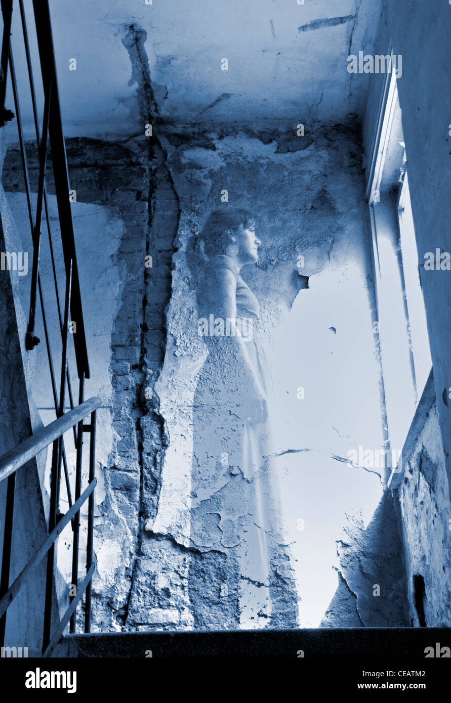 Ghostly young woman standing in ruined corridor looking through window Stock Photo