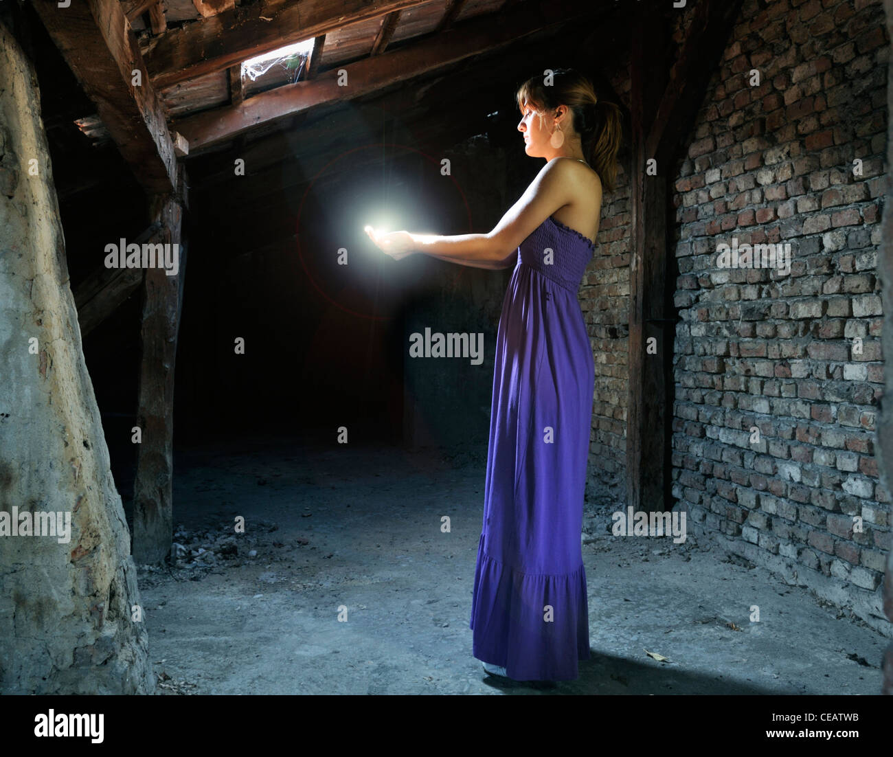 Young woman standing in attic capturing light between hands Stock Photo