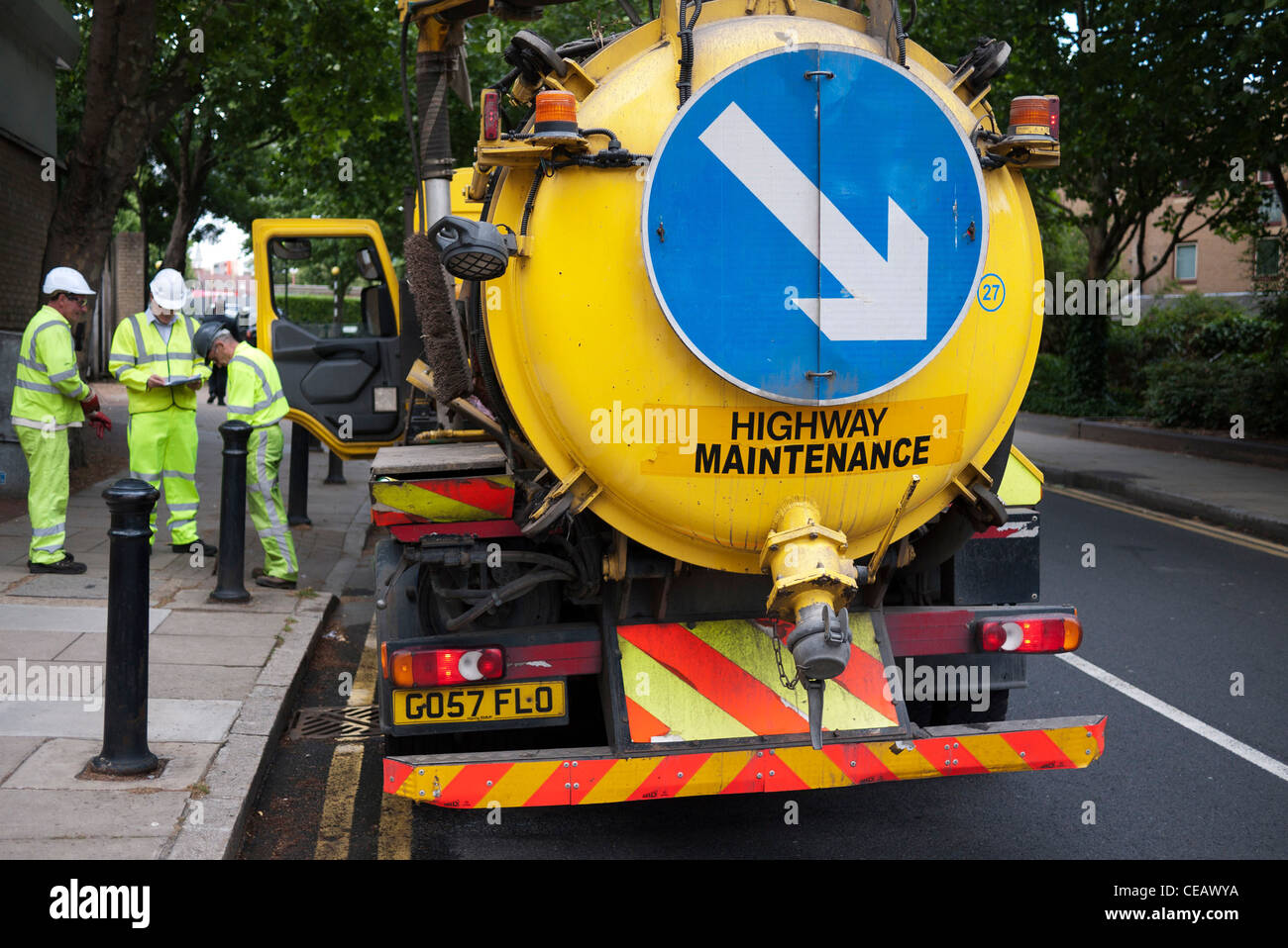 Highway maintenance workers and their vehicle working in London. This water truck inspecting pipelines in the road has a large blue sign with a white arrow to direct other road users around the wide vehicle. Stock Photo