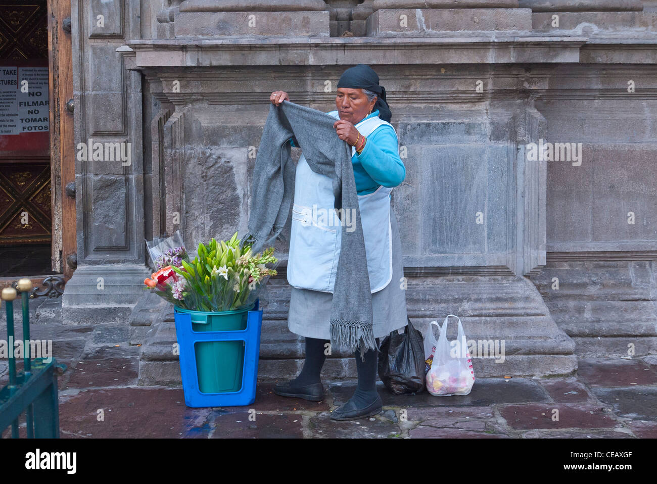 A 60-70 year old indigenous Indian woman prepares to sell her fresh flowers on the street outside a church in Quito, Ecuador. Stock Photo