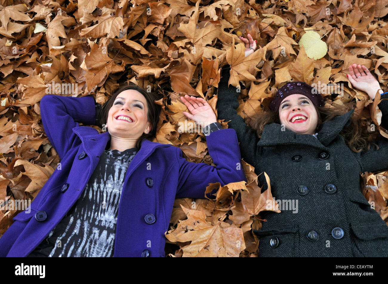 Portrait of a two young woman lying on autumn leaves from a bird's eye view laughing and having fun Stock Photo