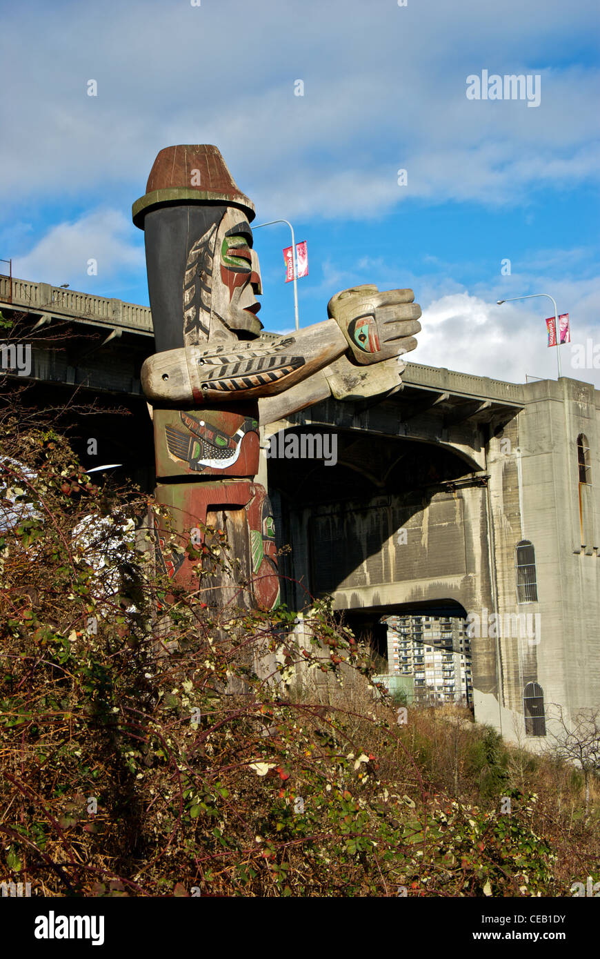 Coast Salish carved wooden welcome figure pole on First Nations land below Burrard Street bridge Vancouver Stock Photo