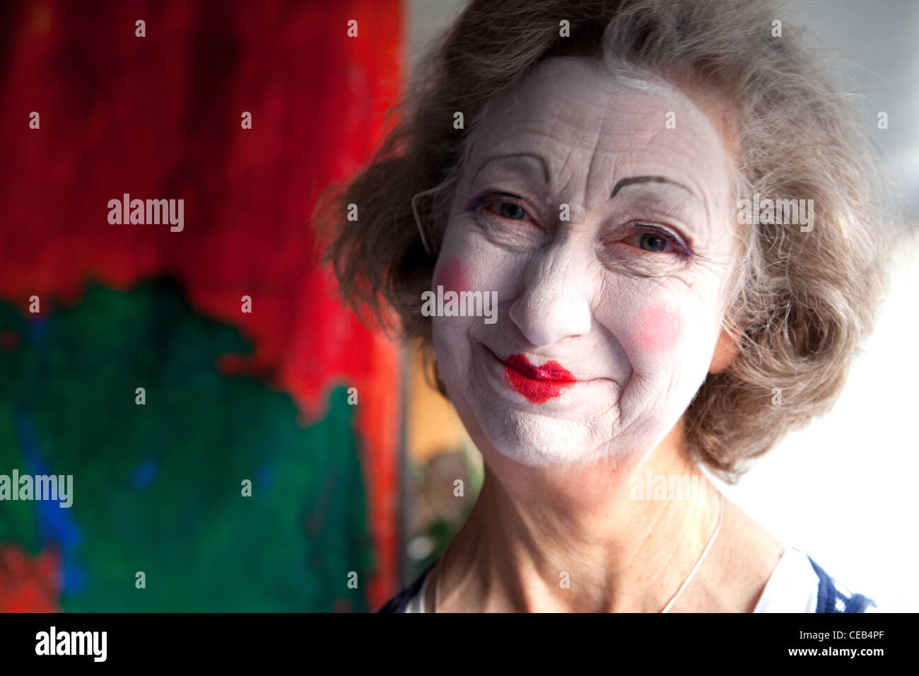Elderly woman smiles to camera, wearing whiteface clown make-up Stock Photo