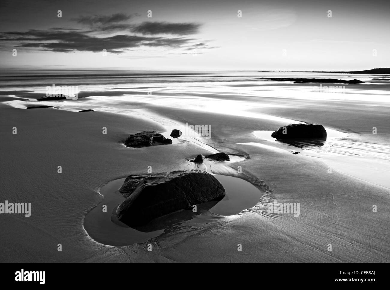 Dawn at Embleton Bay. Rocks left in the sand are surrounded by small pools which are reflecting the dawn light. Stock Photo