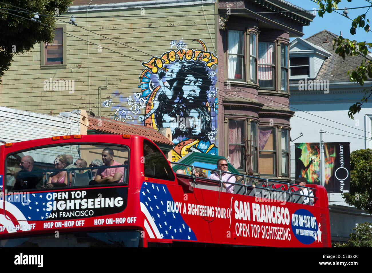 An open top double decker tour bus passing a rock musicians mural