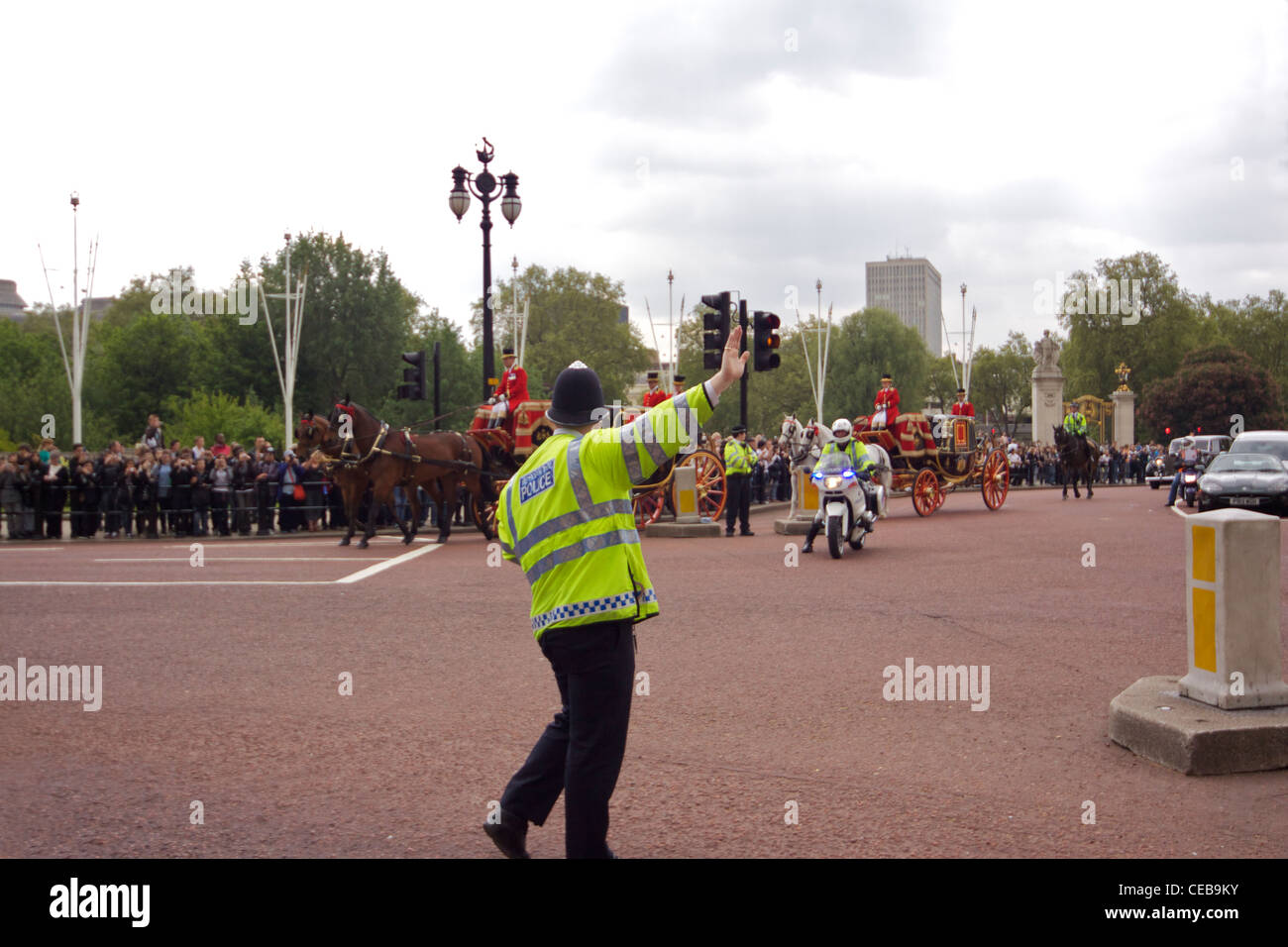 A Metropolitan police officer directs traffic as horses and coaches proceed down the Mall during the 'Changing of the Guard' Stock Photo