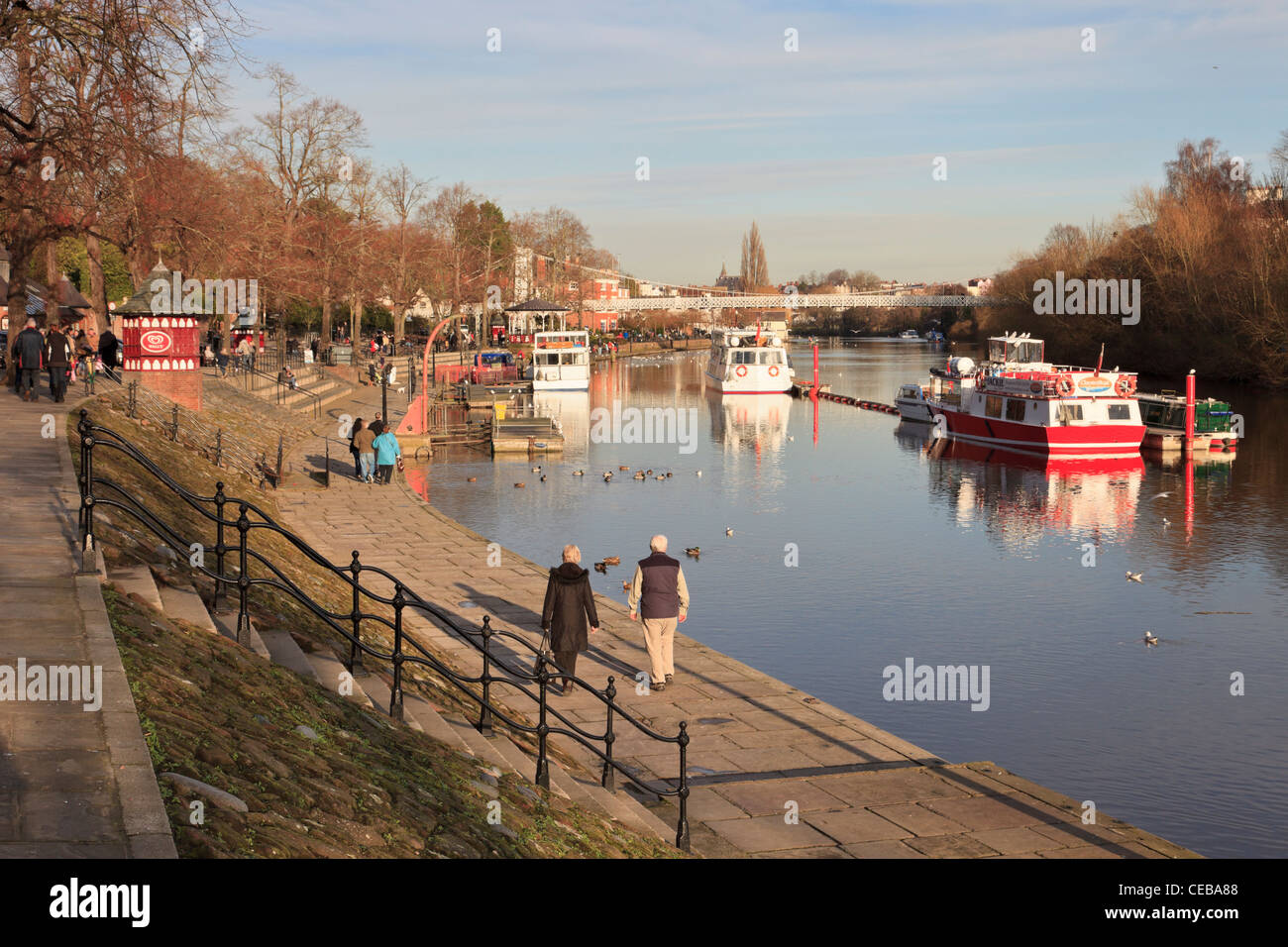 People walking along River Dee riverside walk with pleasure boats by boat landing stage. The Groves Chester Cheshire England UK Stock Photo