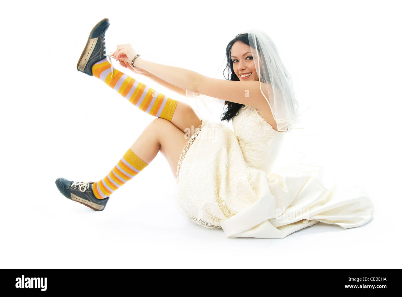 beautiful smiling bride sitting on the floor and putting on old blue trainers Stock Photo
