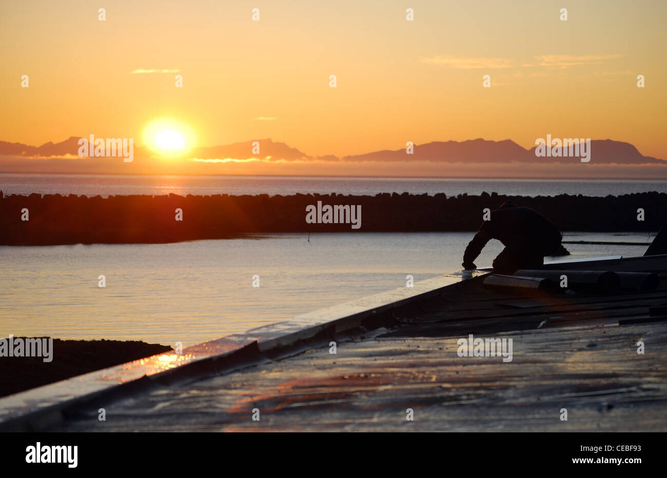 sunset at seaside with mountains silhouette and workman roofing Stock Photo