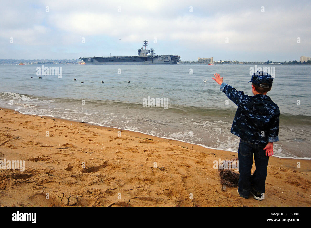 The son of Electrician’s Mate (Nuclear) 1st Class Randall White, assigned to the Nimitz-class aircraft carrier USS Carl Vinson (CVN 70), waves to his father’s ship as it transits San Diego Bay after departing Naval Air Station North Island on a scheduled deployment to the western Pacific region. Stock Photo