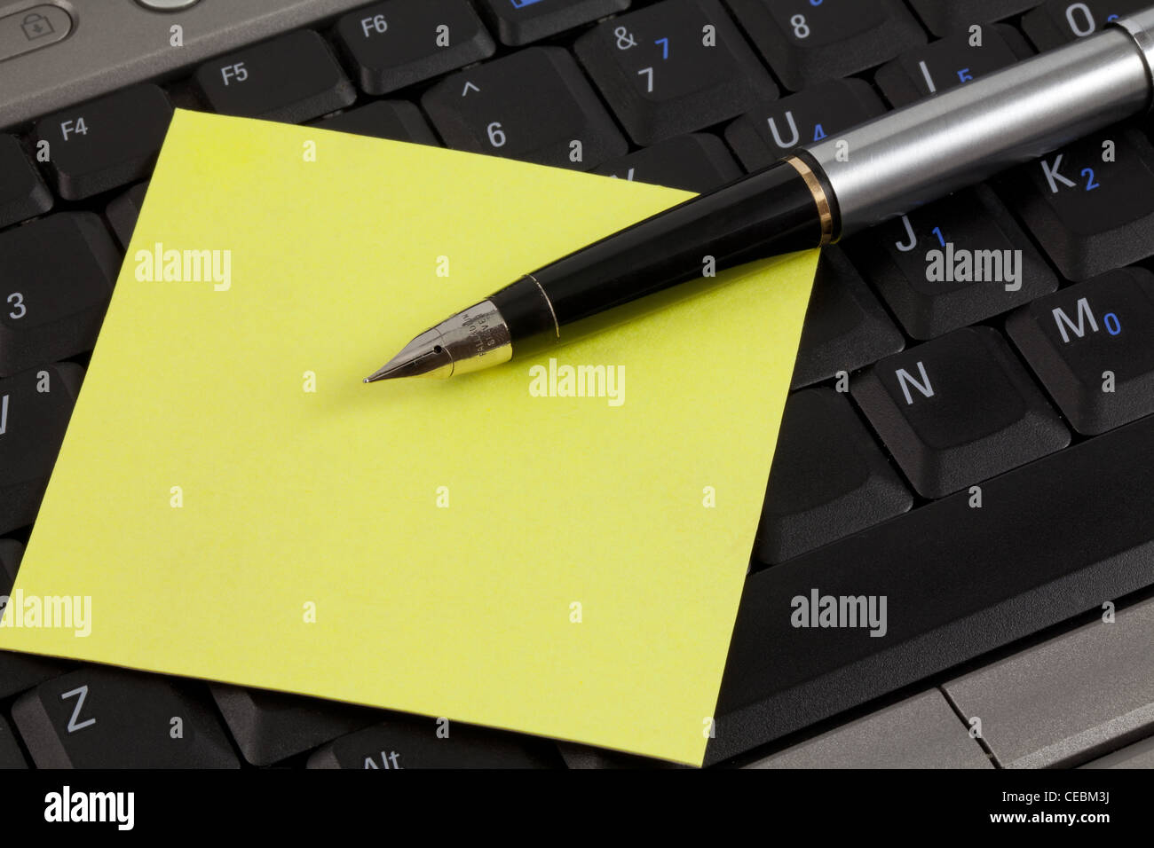 A yellow post it note and a fountain pen on a laptop keyboard. With ...