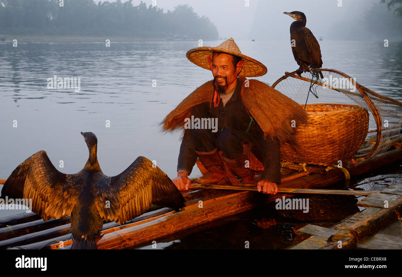 Smiling cormorant fisherman with birds on a bamboo raft on the Li river at dawn Xingpingzhen Yangshuo, Guilin, Guangxi China Stock Photo