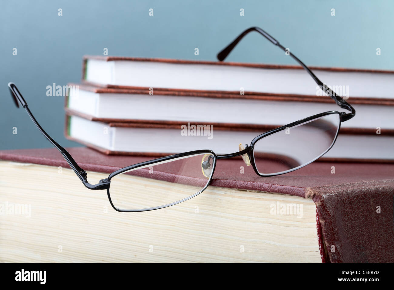 glasses hang down from a pile of books in hard cover Stock Photo