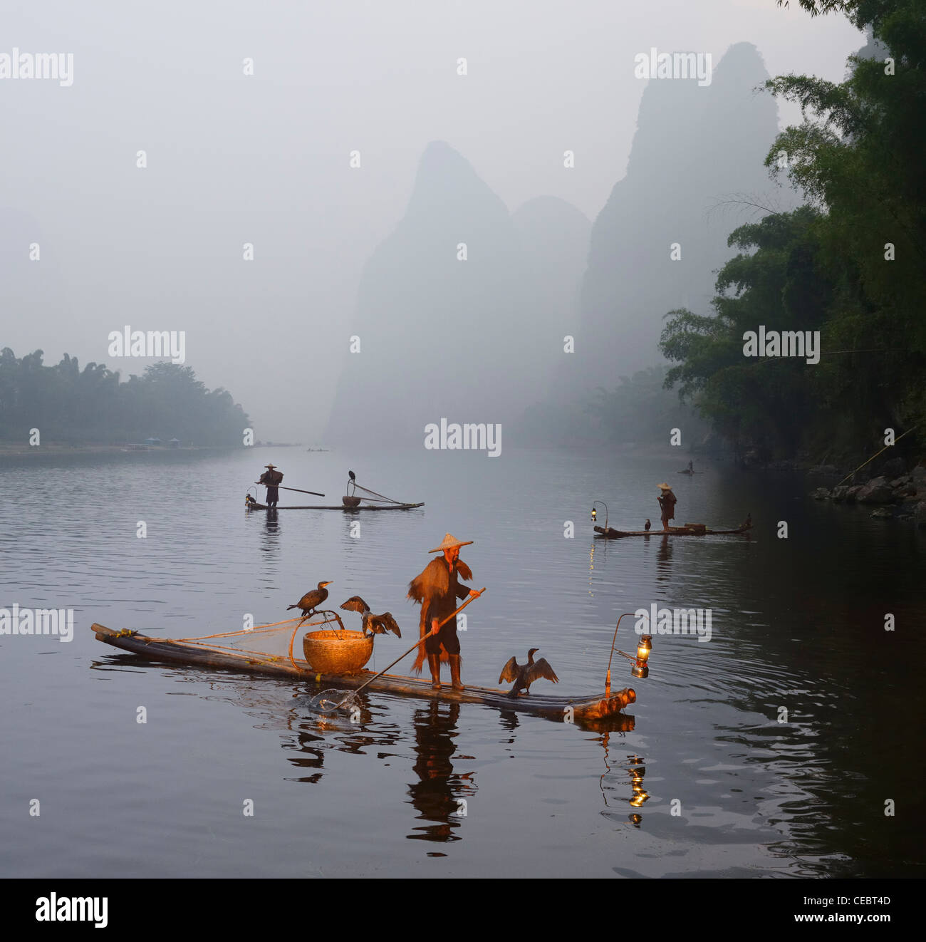 Cormorant fishermen paddling bamboo raft at dawn on the Li river with Karst mountain peaks Xingpingzhen Yangshuo, Guilin, Guangxi China Stock Photo