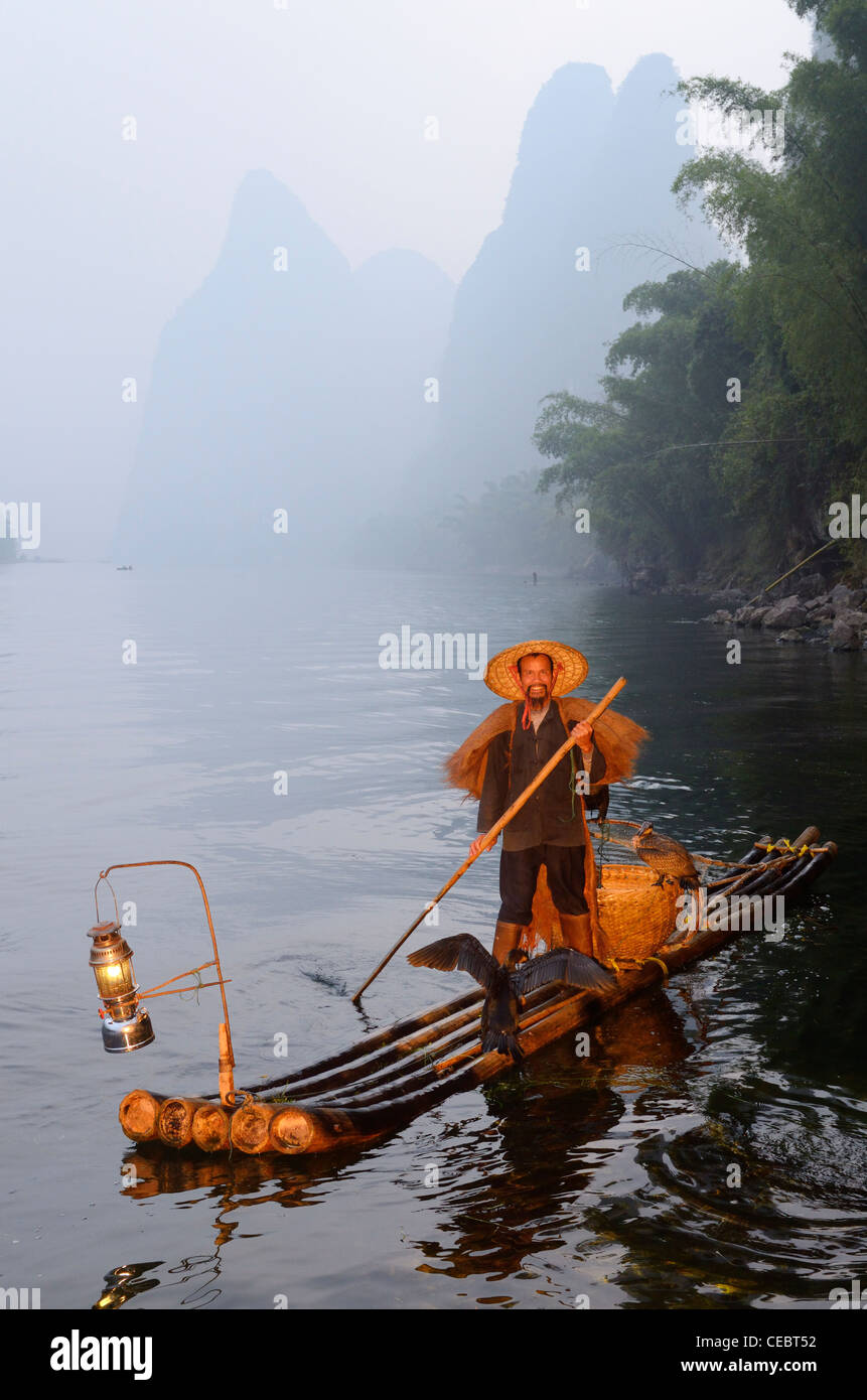 Cormorant fisherman paddling bamboo raft on the Li river with Karst mountain peaks Xingpingzhen Yangshuo, Guilin, Guangxi China Stock Photo