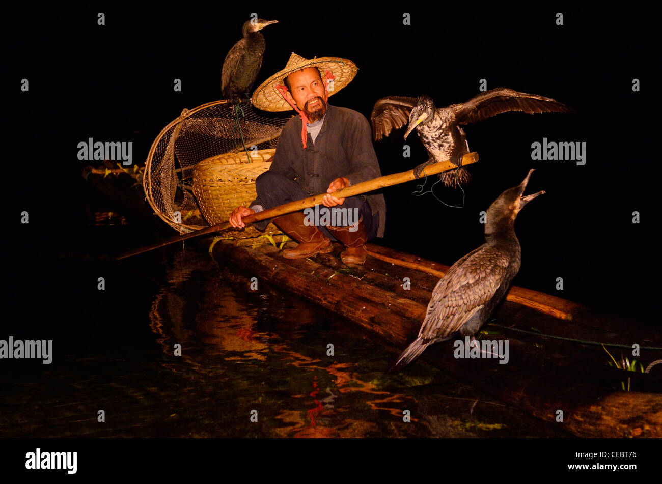 Cormorant fisherman holding bird on a pole on a bamboo raft on the Li or Lijiang river at night Xingpingzhen Yangshuo, Guilin, Guangxi China Stock Photo