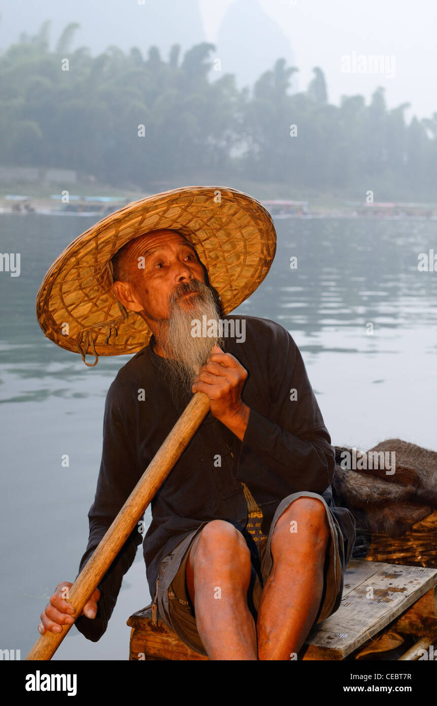 Proud Cormorant fisherman on a bamboo raft on the Li river with Karst mountain peaks Xingpingzhen Yangshuo, Guilin, Guangxi China Stock Photo