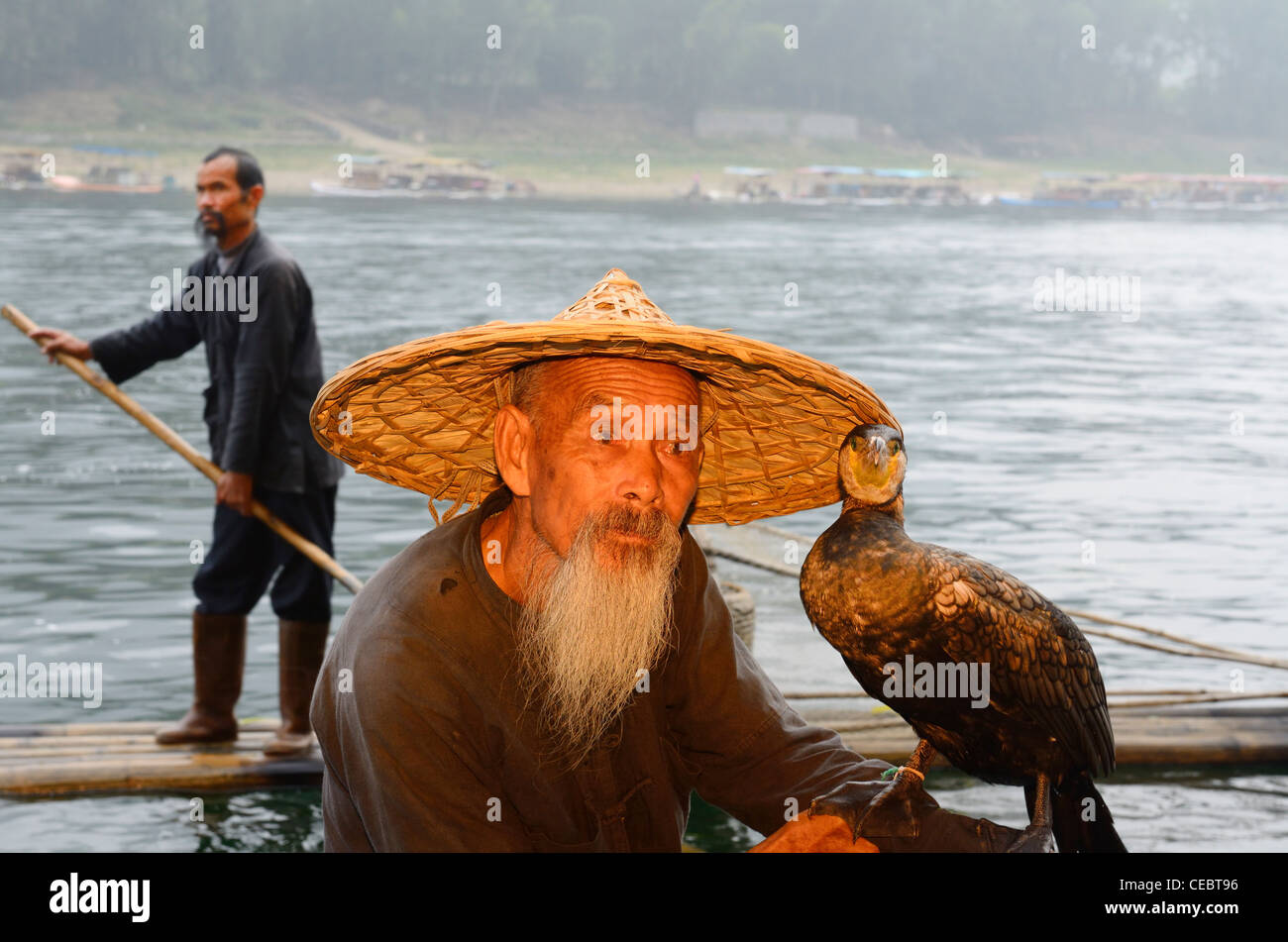 Cormorant fisherman holding bird and another paddling past on the Li or Lijiang river near Xingpingzhen Yangshuo, Guilin, Guangxi China Stock Photo