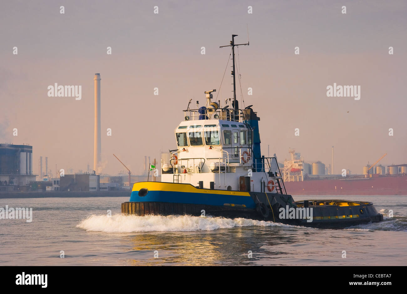 Tug on the river passing by in the sun with industry in background Stock Photo