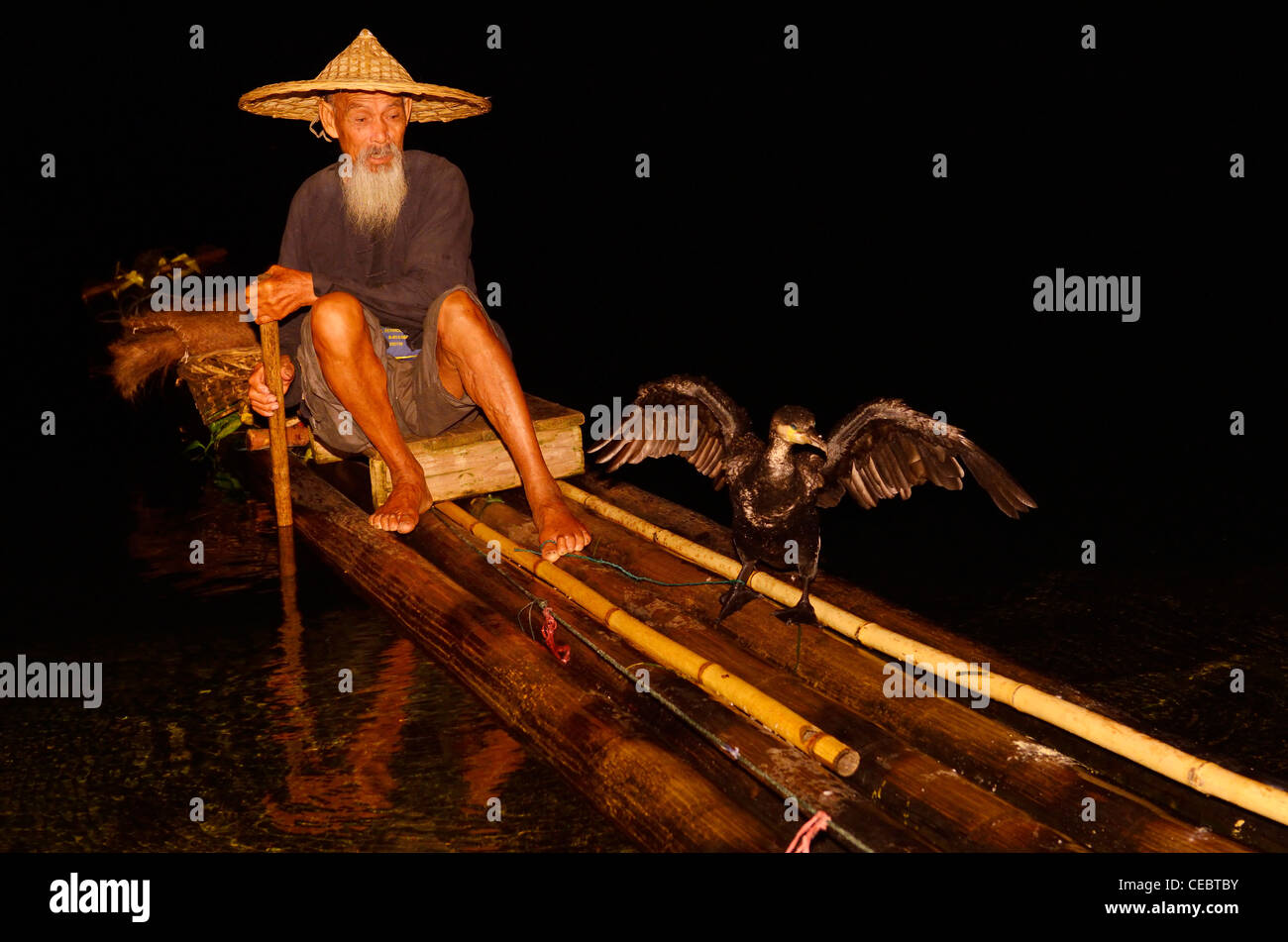 Cormorant fisherman holding bird on a string on a bamboo raft on the Li river at night Xingpingzhen Yangshuo, Guilin, Guangxi China Stock Photo