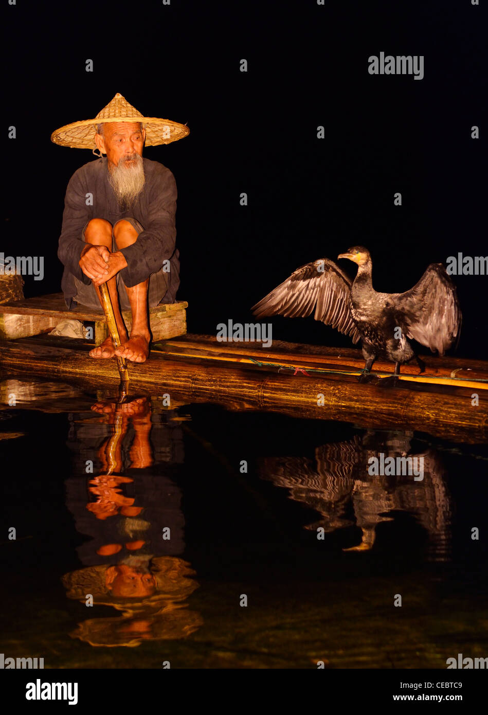 Cormorant fisherman and bird with spread wings reflected in the Li river at night from a bamboo raft Xingpingzhen Yangshuo, Guilin, Guangxi China Stock Photo
