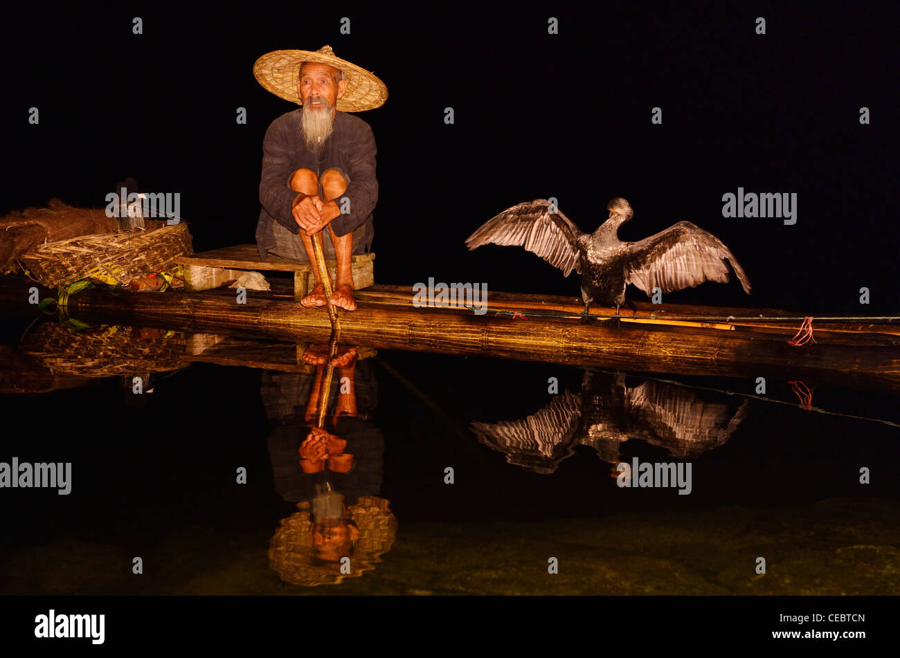 Cormorant fisherman and bird with spread wings reflected in a calm Li river at night from a bamboo raft Xingpingzhen Yangshuo, Guilin, Guangxi China Stock Photo