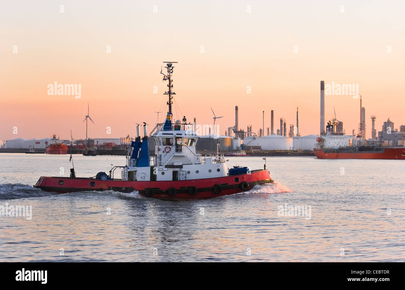 Tug passing by at high speed on the river at colorful sunset - industrial pollution is painting the sky Stock Photo