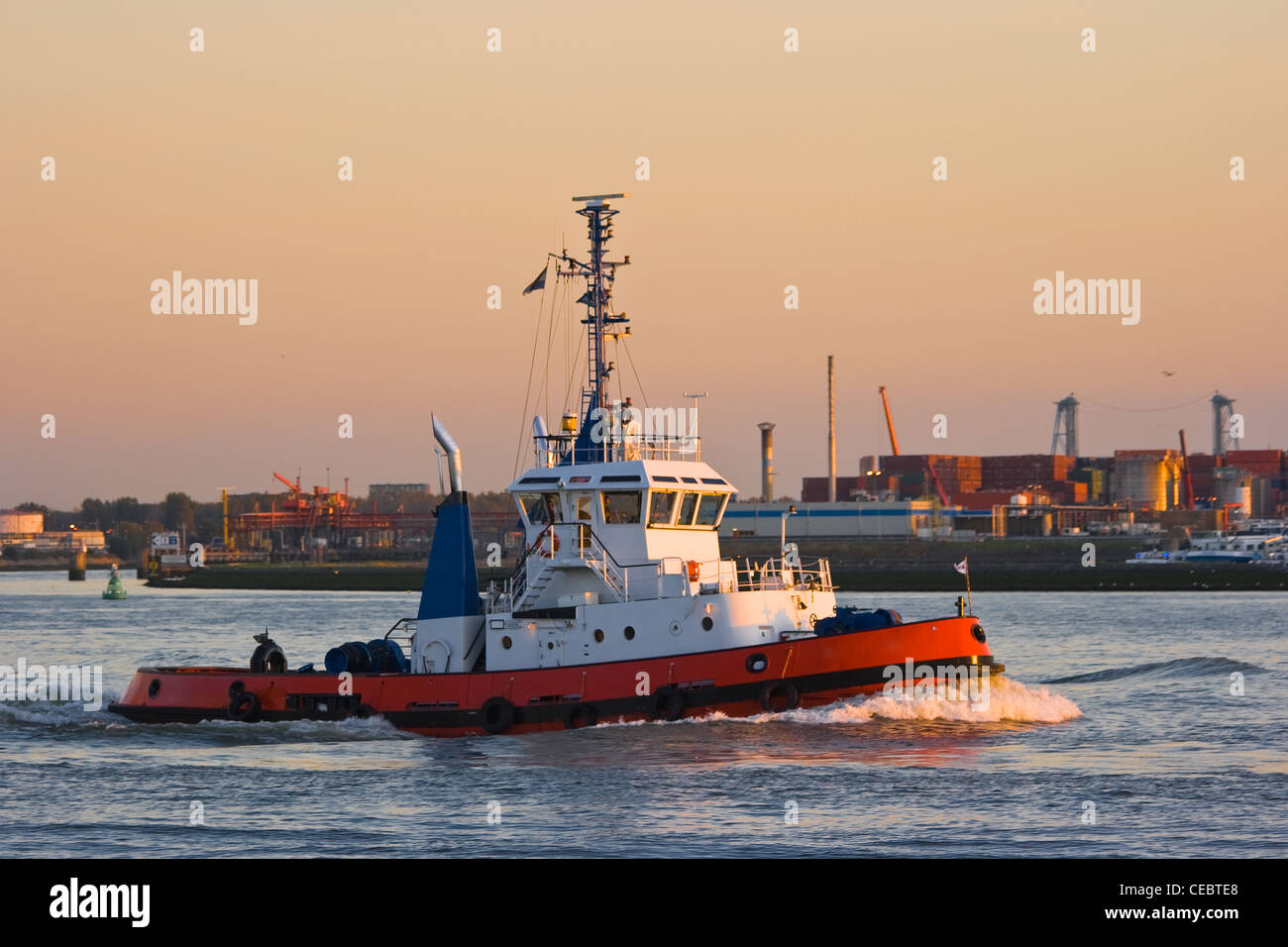 Tug passing by on the river at sunset with industry in background Stock Photo