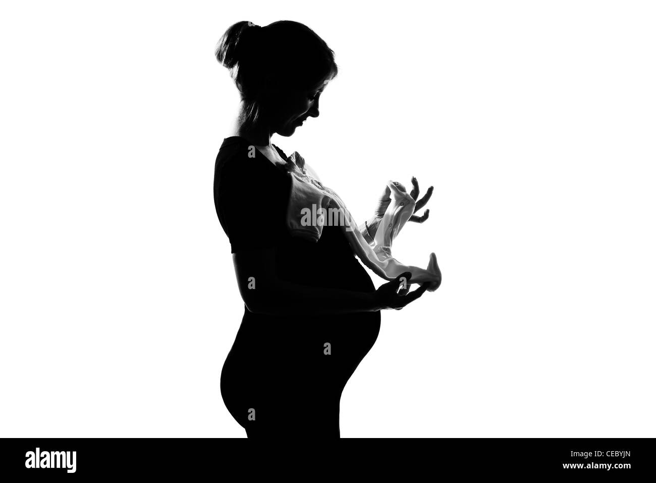 one beautiful caucasian pregnant woman holding baby clothes in silhouette on studio isolated white background Stock Photo