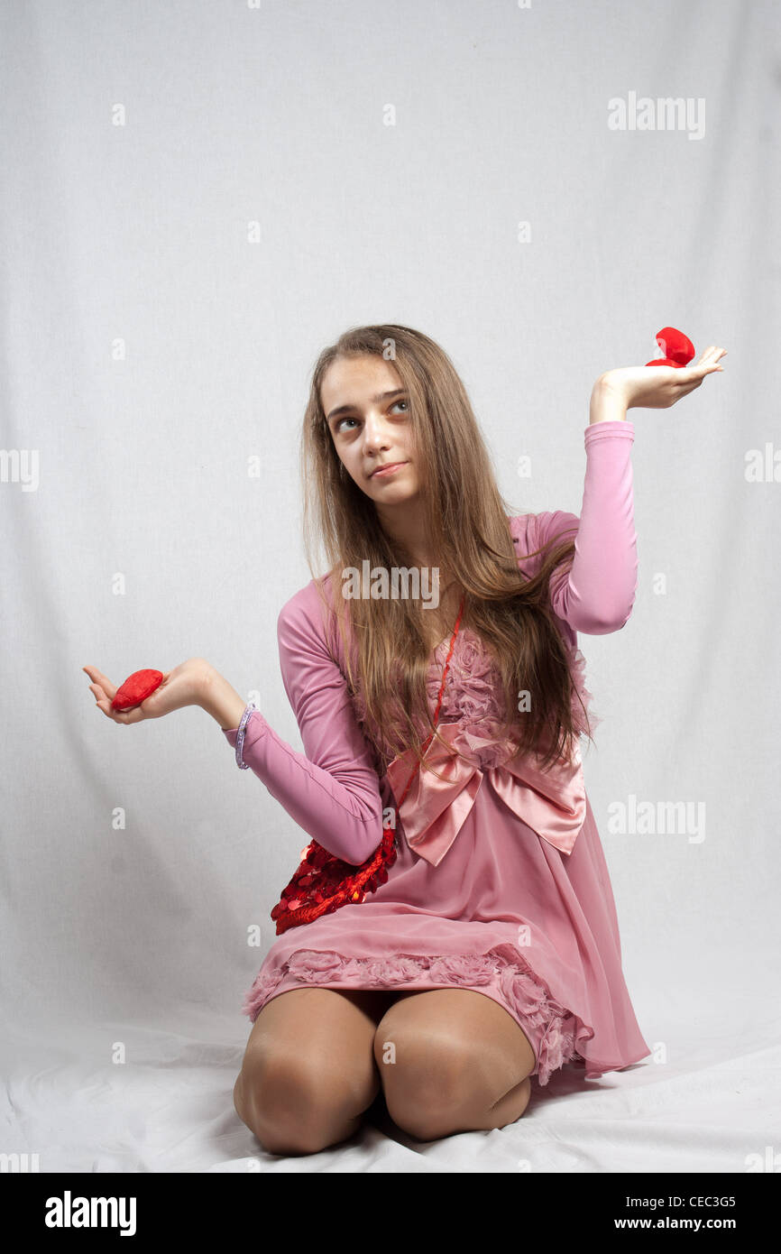 Teenage girl in pink weighing two valentines gifts Stock Photo