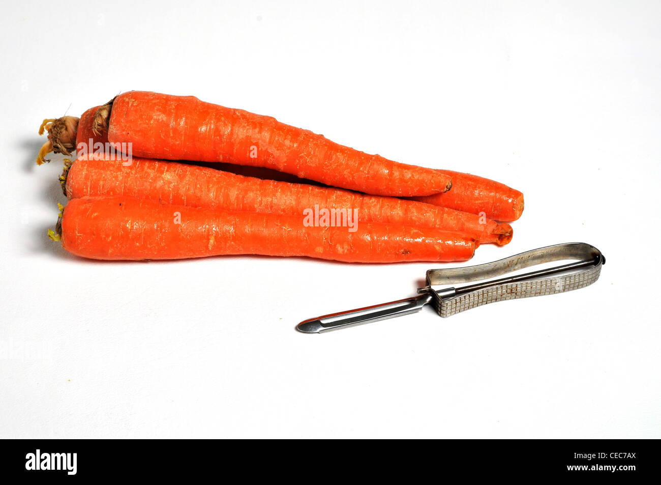 Carrots and a potato peeler are laying on a plain white background. Stock Photo