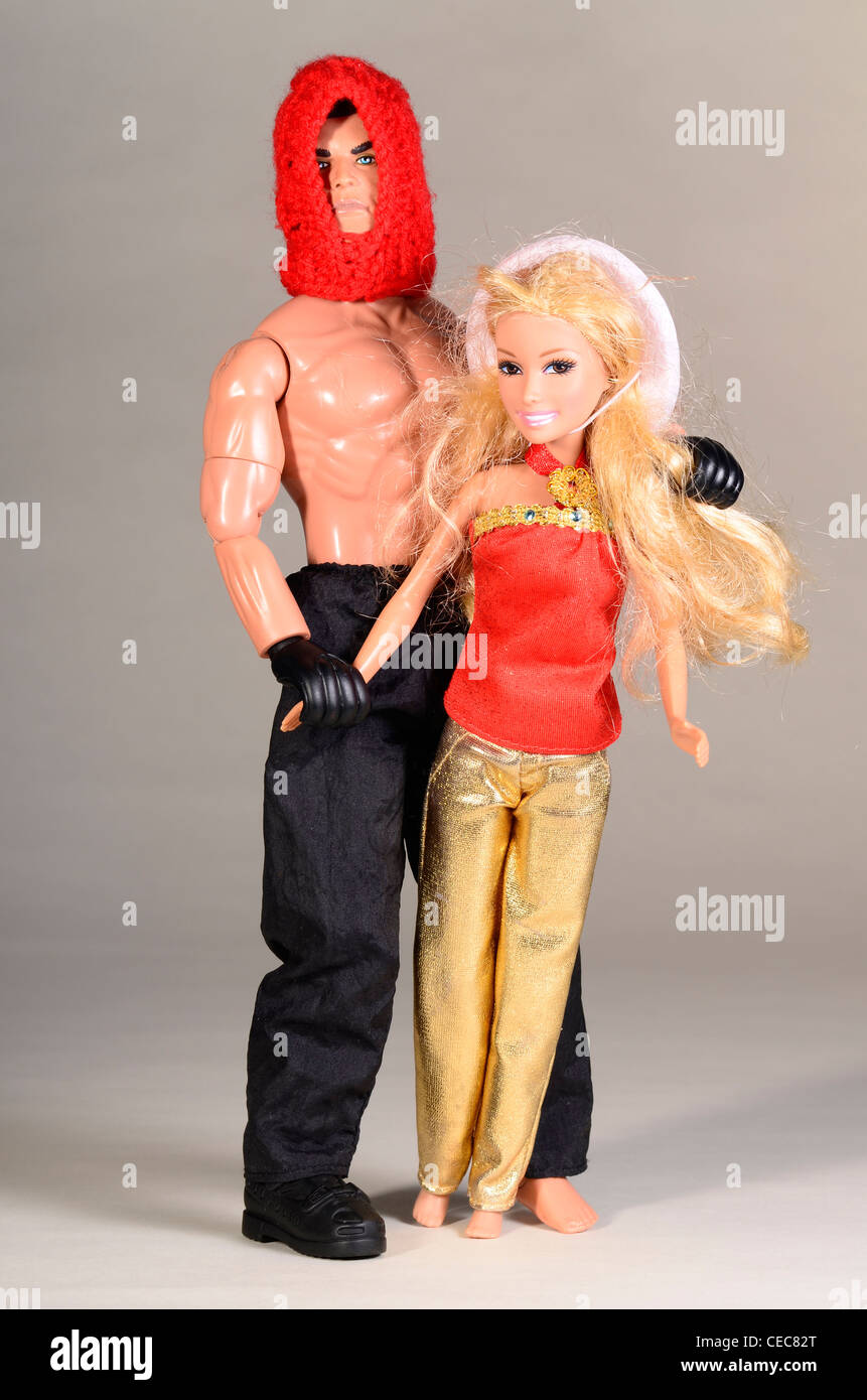 action man doll wearing bright red woolen balaclava with little cowgirl dolly wearing gold trousers Stock Photo