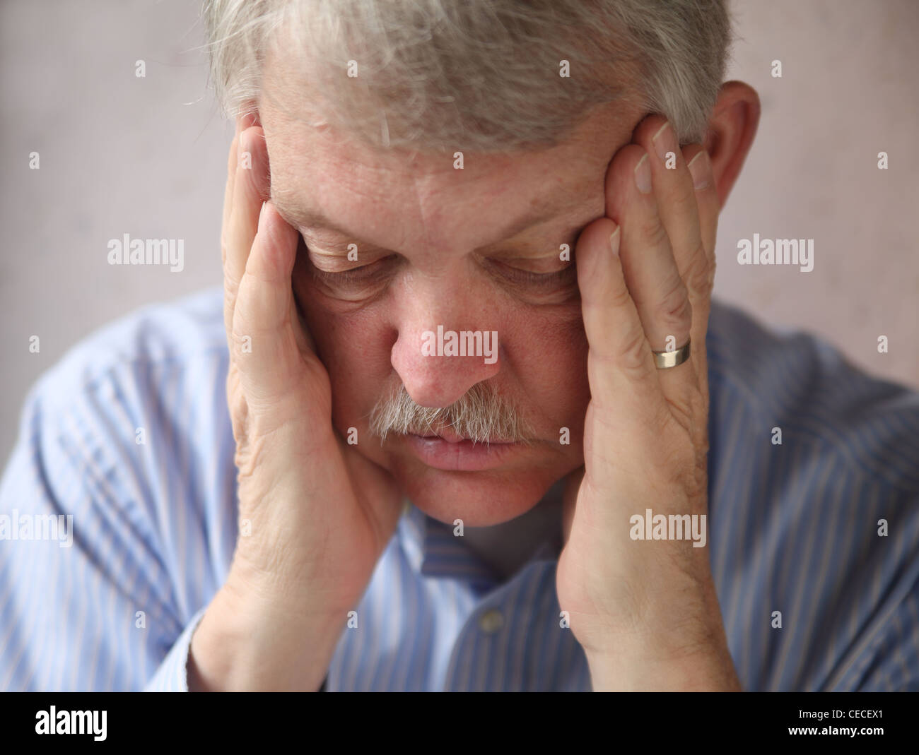 an older man with hands supporting his head, looking down Stock Photo