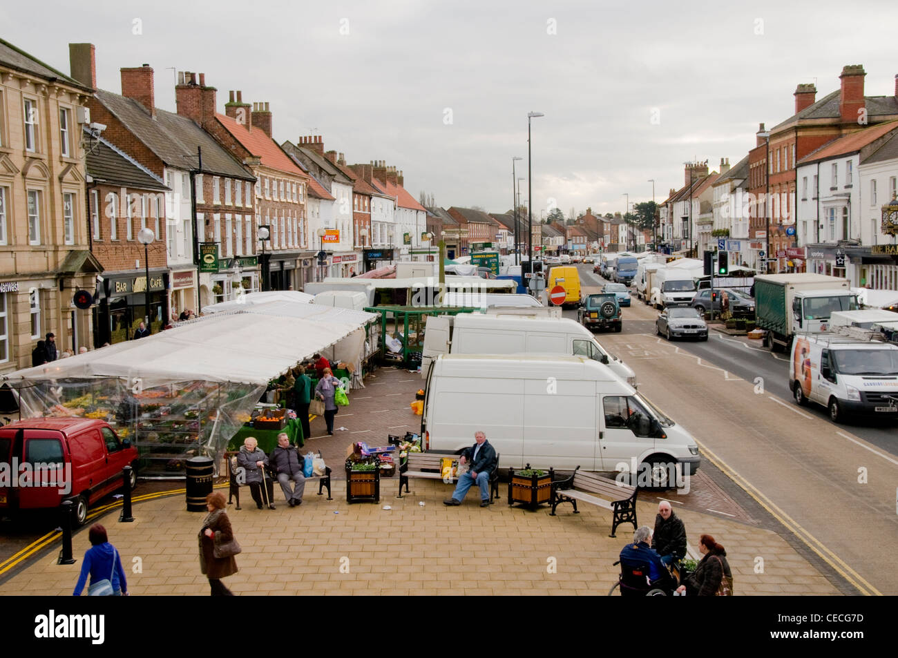 Busy bustling scenic town (Northallerton High Street) on market day (stalls, people shopping, vehicles on road, shops) - North Yorkshire, England, UK. Stock Photo