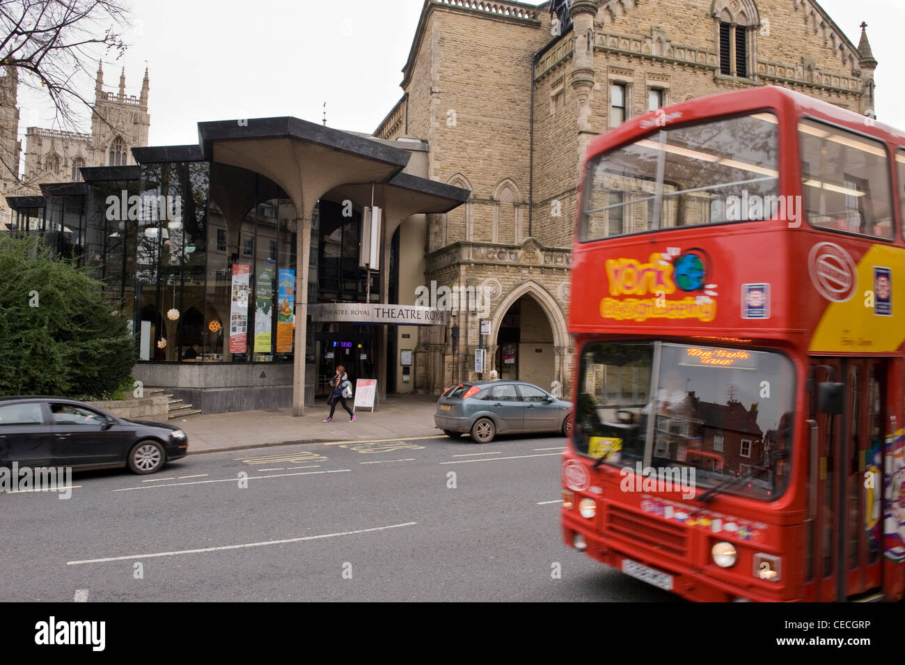 Red sightseeing tour bus passing The Theatre Royal (historic building with Gothic frontage & Modernist extension) - York, North Yorkshire, England. Stock Photo