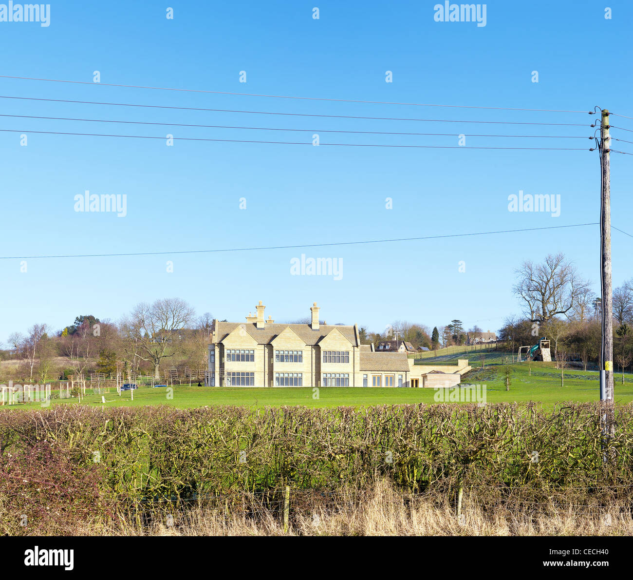 Hedge and electricity wires framing a newly built english mansion. Stock Photo