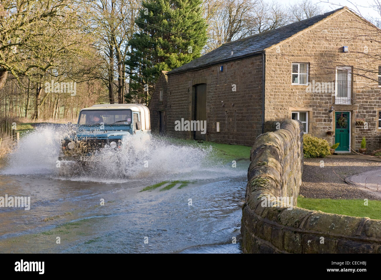 Flooding - Land Rover Defender driving & splashing through deep flood water on flooded rural road after torrential rain - North Yorkshire, England, UK Stock Photo