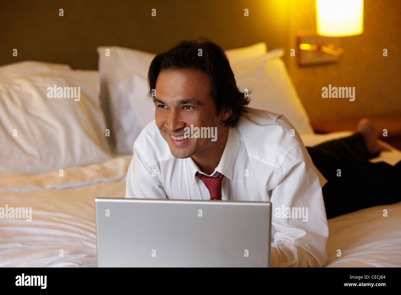 man lying on bed smiling while working on lap top Stock Photo - Alamy