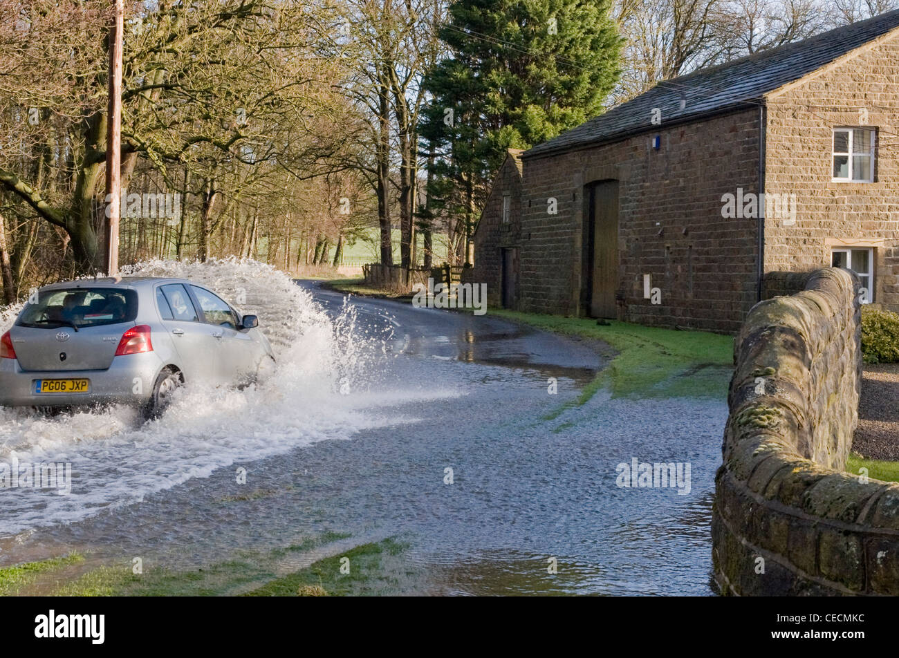 Flooding - silver car (Toyota) driving & splashing through deep flood water on flooded rural road after torrential rain - North Yorkshire, England, UK Stock Photo