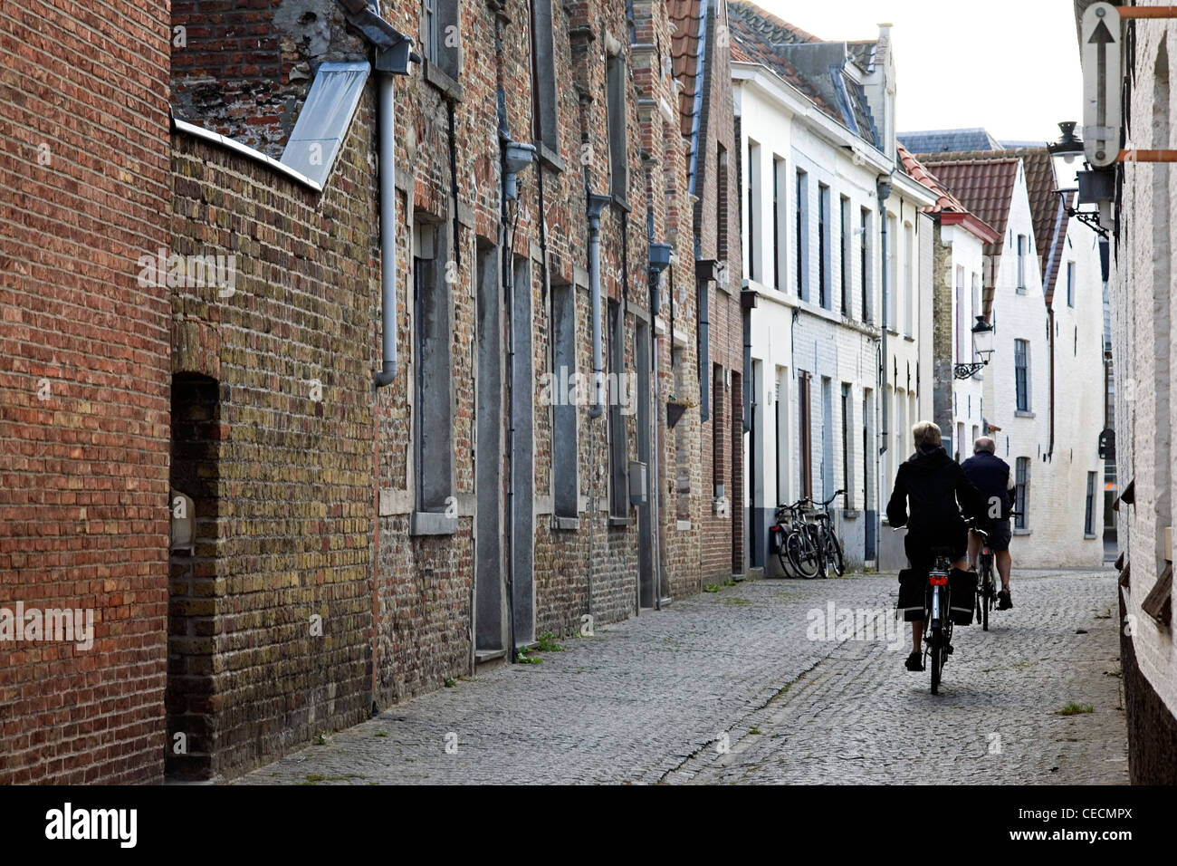 Couple cycling along narrow street in Bruges, Belgium Stock Photo