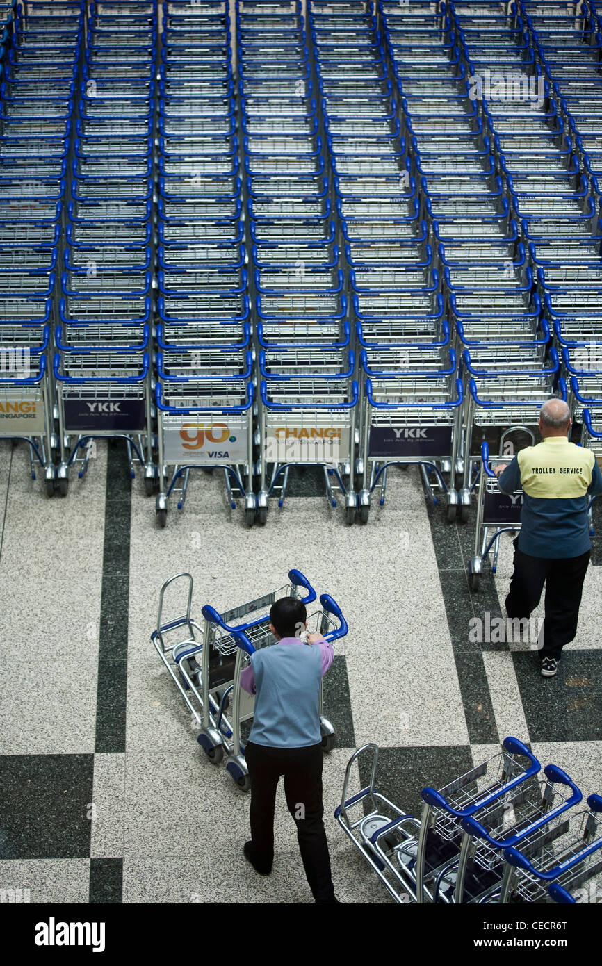 Airport workers arrange baggage trolleys in the arrivals area of Changi