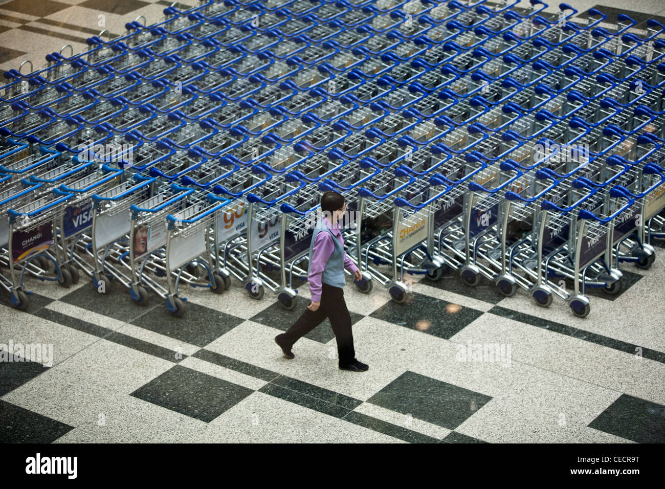 An airport worker arranges baggage trolleys in the arrivals area of