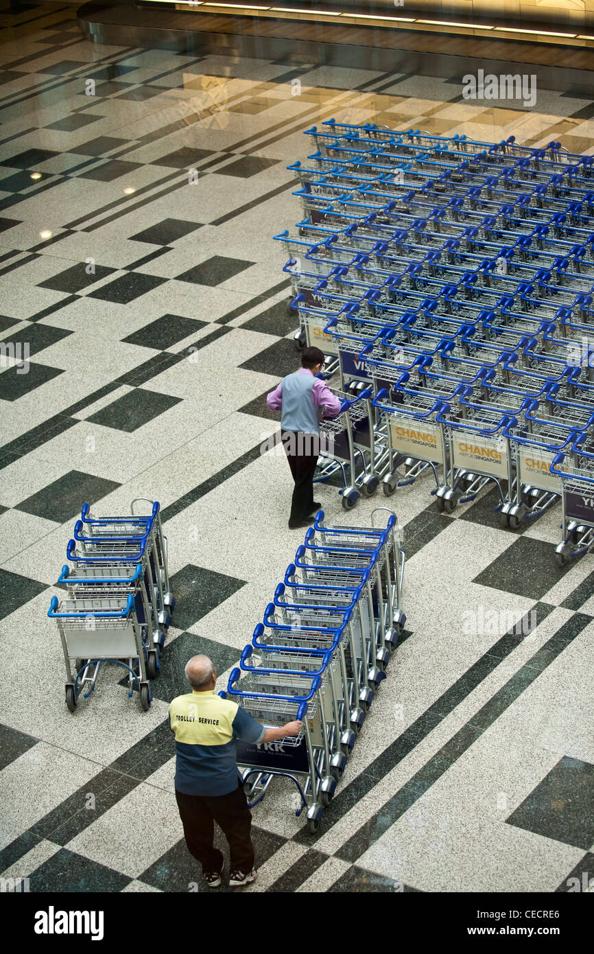 Airport workers arrange baggage trolleys in the arrivals area of Changi