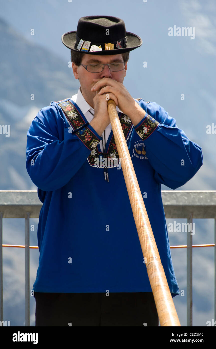 Vertical close up portrait of a traditionally dressed Swiss man playing the Alpine horn on a sunny day. Stock Photo