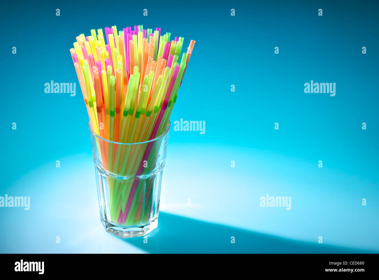 Multicolor flexible straws in the glass in spot of light isolated on blue background Stock Photo