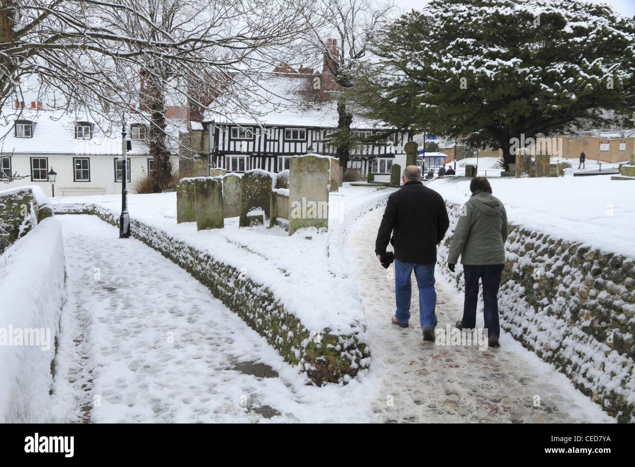 Two people couple husband and & wife walking through a graveyard  in winter snow snowy Old Town Eastbourne, East Sussex, England Stock Photo
