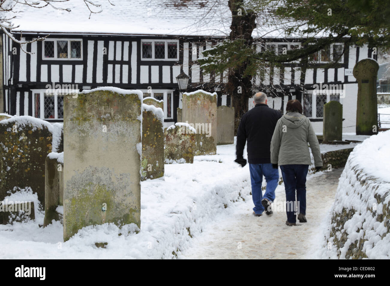 Two people couple husband and & wife walking through a graveyard  in winter snow snowy Old Town Eastbourne, East Sussex, England Stock Photo