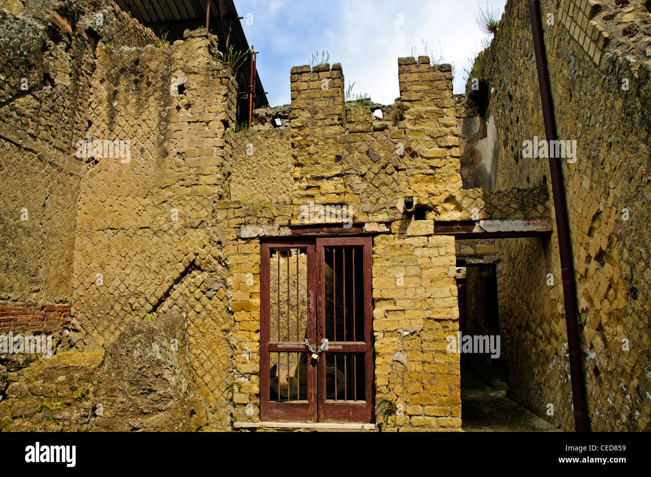 The excavated ruins of a two storey building containing the remains of two grindstones behind the gate, Herculaneum Stock Photo
