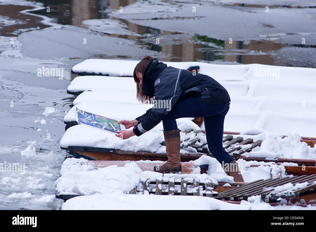A student clearing the snow off the punts in Cambridge, England. Stock Photo